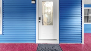 A white door with a glass panel and a decorative design, set in a blue house with a red porch. - New Listing!  Charming House at The Blue Anchor Hotel.  4 Kings, sleeps 8. (Houghton Lake)