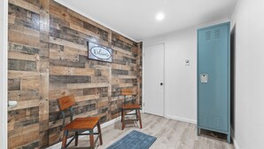 A room with a wooden wall, two wooden chairs, a blue rug, a white door, and a blue locker. - New Listing!  Charming House at The Blue Anchor Hotel.  4 Kings, sleeps 8. (Houghton Lake)