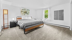 A modern bedroom with a bed, bedside table, lamp, and artwork. - New Listing!  Charming House at The Blue Anchor Hotel.  4 Kings, sleeps 8. (Houghton Lake)