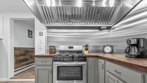 A modern kitchen with a stainless steel range hood, a built-in oven, and a wooden countertop. - New Listing!  Charming House at The Blue Anchor Hotel.  4 Kings, sleeps 8. (Houghton Lake)