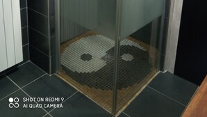 Une cabine de douche fermée par des parois en verre, dotée d’un pommeau de douche à main, d’un porte-serviettes et d’un tapis de sol à motifs.