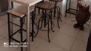 Une cuisine moderne avec une table en bois, quatre chaises en métal, un évier en acier inoxydable, un réfrigérateur et un coq décoratif en céramique.