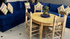 A modern living room with a blue sofa, wooden chairs, a round wooden table, and a decorative ceiling light. - SINIM HOUSE (Taghazout)