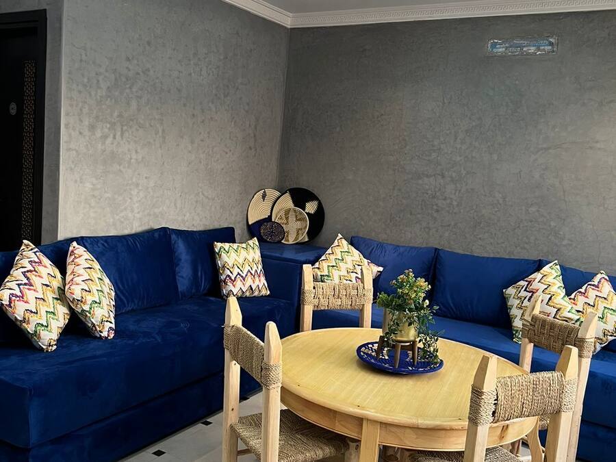 Un salon moderne avec un canapé bleu, des chaises en bois, une table ronde en bois et un luminaire décoratif au plafond.