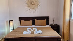A neatly made bed with a yellow rug, a wall-mounted decorative piece, and a bedside table with a lamp. - SINIM HOUSE (Taghazout)