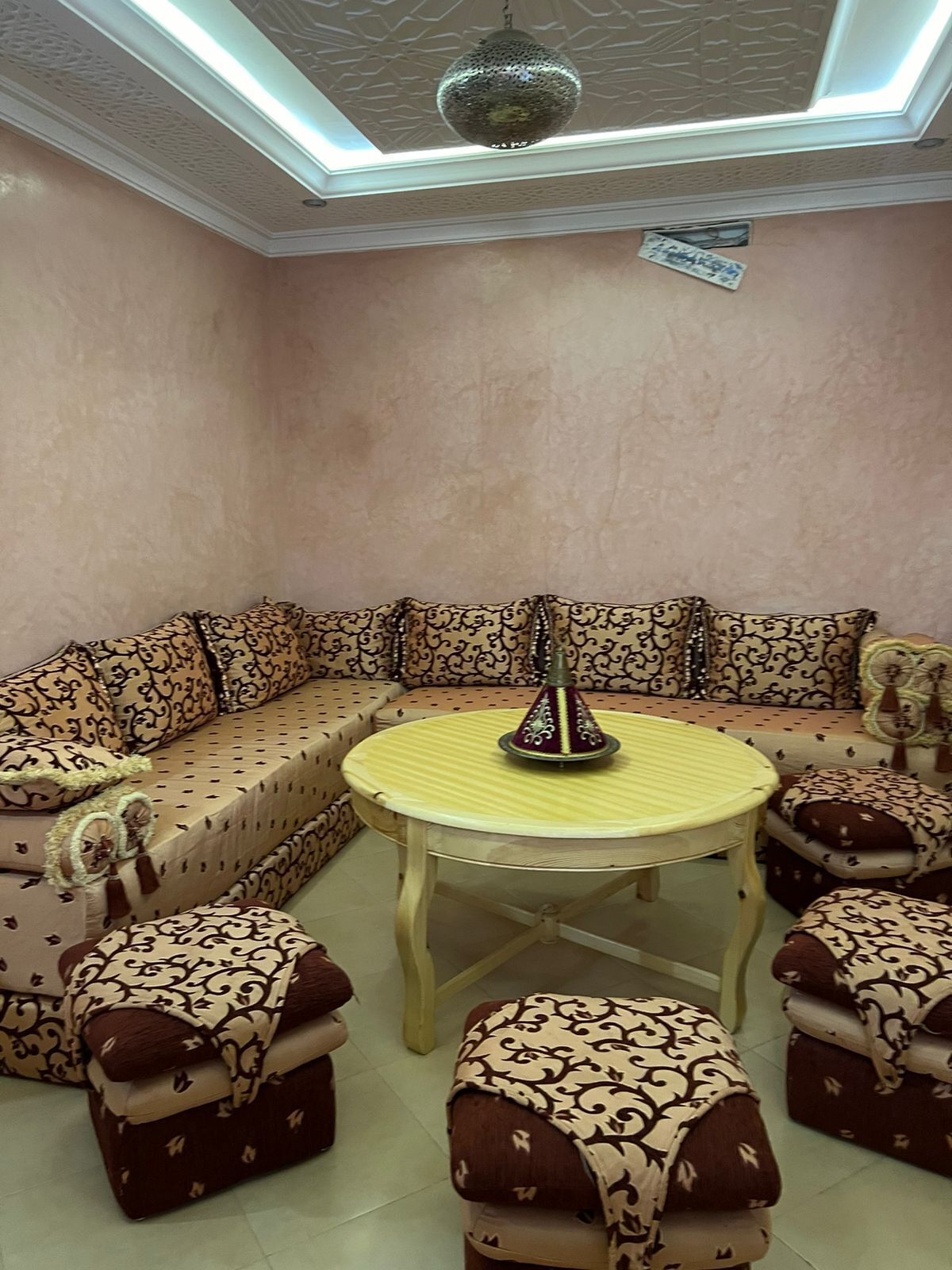 A room with a beige patterned sofa, matching ottomans, and a round table with a decorative centerpiece.