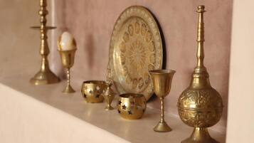 A collection of brass decorative items on a shelf, including a plate with a floral design, a tall stand, and several smaller bowls and cups.