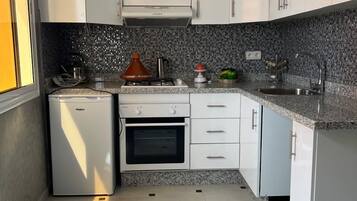 Cozinha compacta com armários brancos, forno embutido, geladeira pequena e painel de azulejos.
