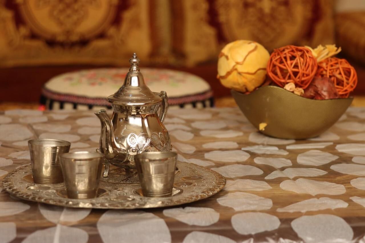 A traditional tea set with four cups and a teapot on an ornate tray, accompanied by a bowl of sweets and a decorative plate in the background.