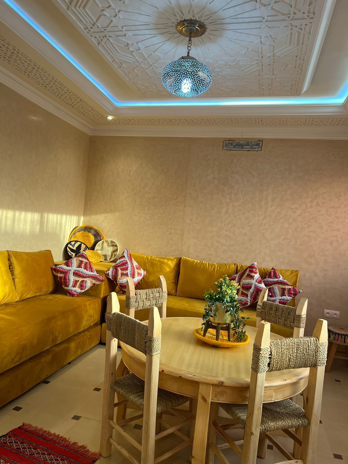 A dining area with a round wooden table, woven chairs, and a yellow sofa with patterned cushions.