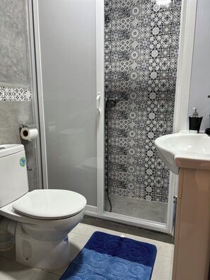A bathroom with a toilet, a shower with patterned tiles, and a sink. - SINIM HOUSE (Taghazout)