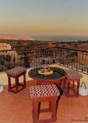 A balcony with a round table and four wooden stools with patterned cushions. - SINIM HOUSE (Taghazout)
