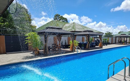 A swimming pool with a water feature, surrounded by covered seating areas and potted plants.