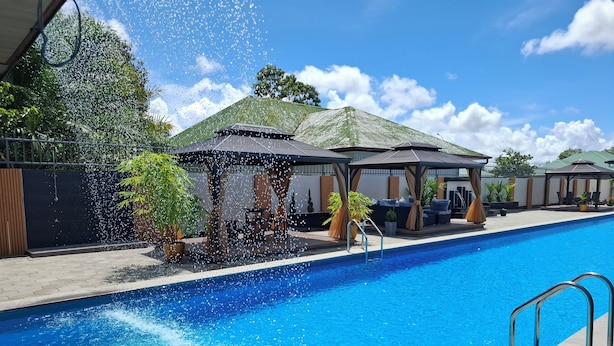 Una piscina con fuente acuática, rodeada de zonas de estar cubiertas y plantas en macetas.