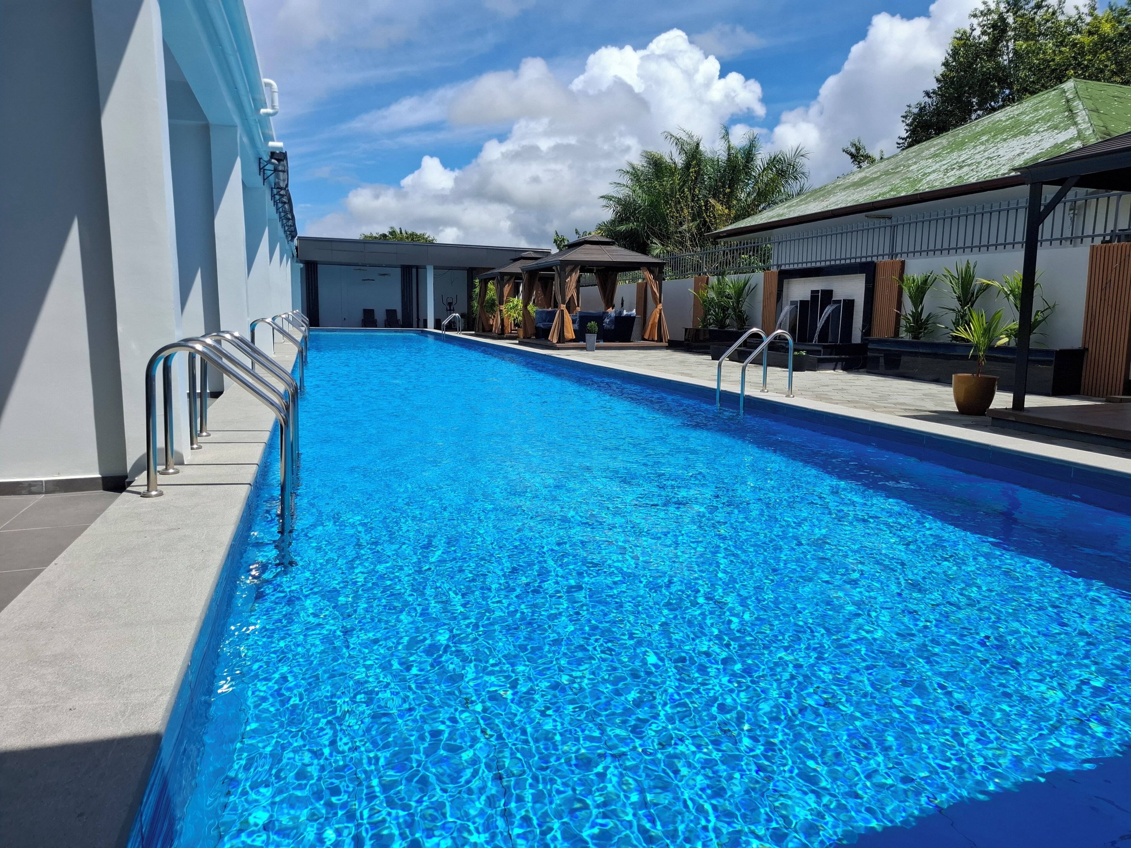 Piscina com grades de metal, área de estar coberta e plantas em vasos.
