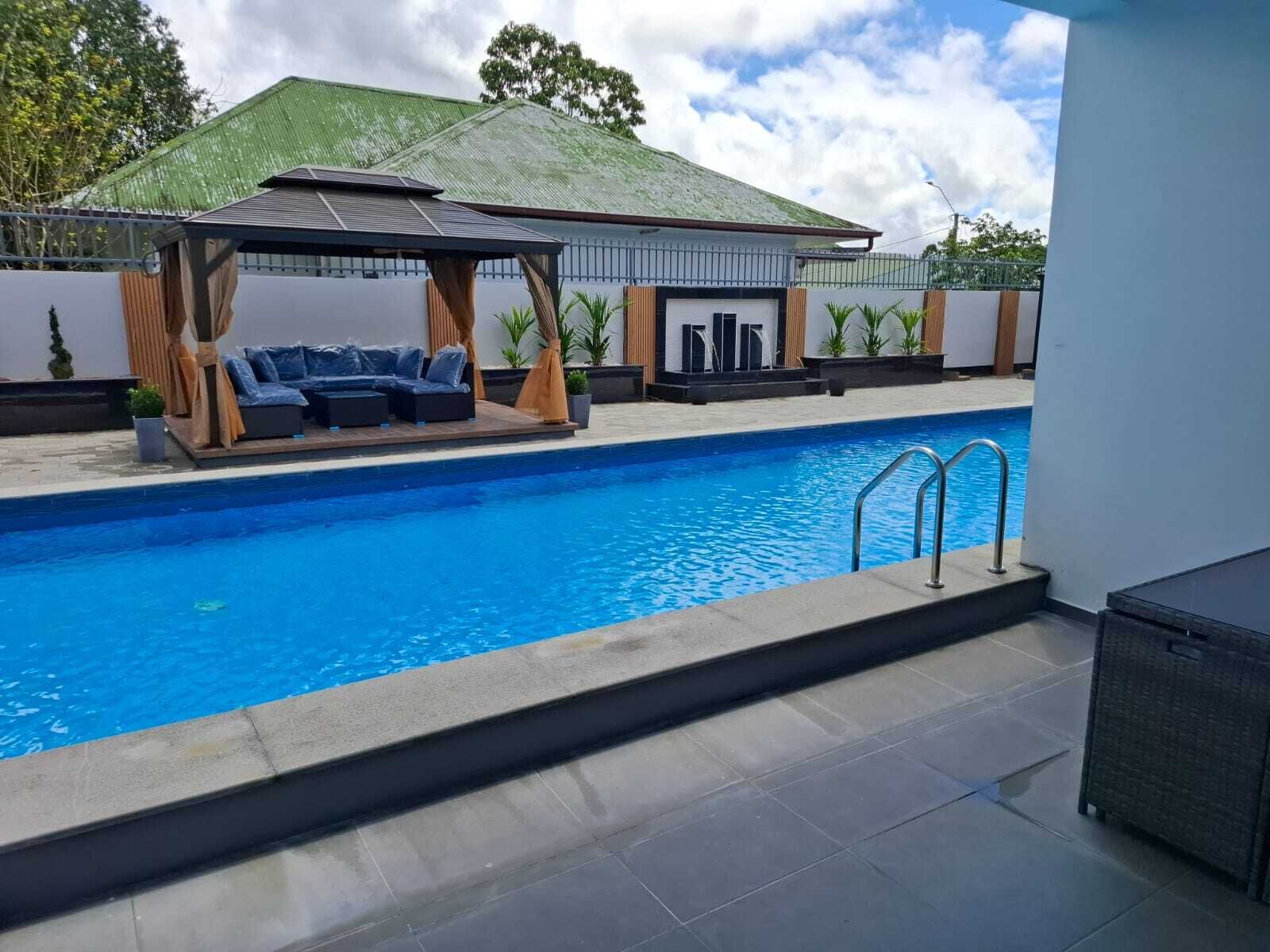 Ein Schwimmbad mit überdachter Liegefläche und einem Gebäude im Hintergrund.