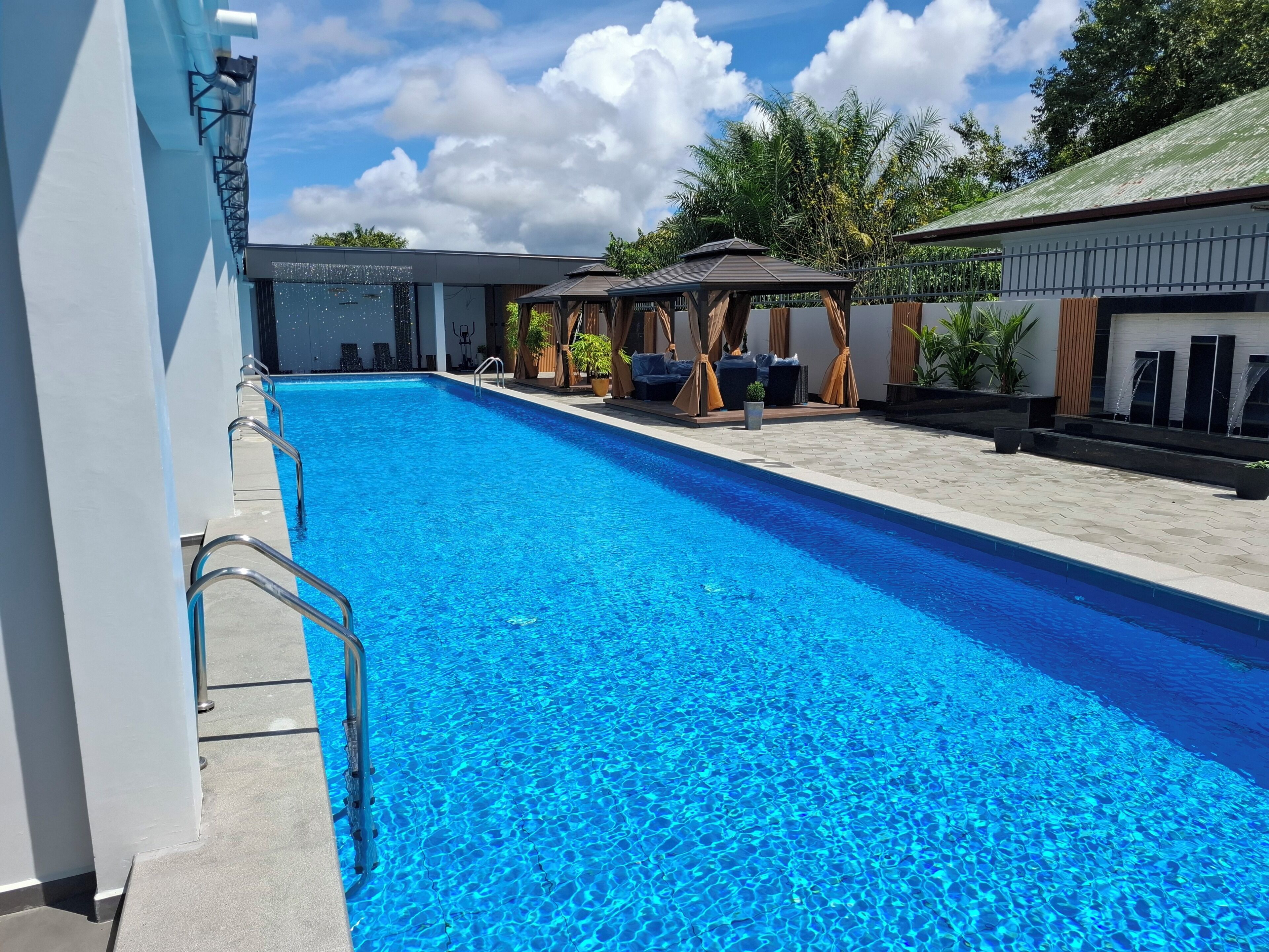 A swimming pool with clear blue water, surrounded by lounge chairs and a covered seating area.