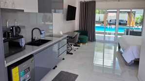 A modern hotel room with a kitchenette, a bed, a pool view, and a flat-screen TV. - ANIRA Hotel & Suites (Lelydorp)