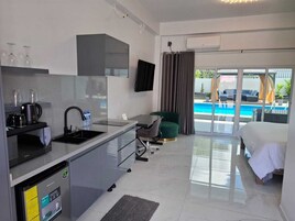 Una habitación de hotel moderna con kitchenette, una cama, vistas a la piscina y un televisor de pantalla plana.