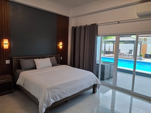 Una habitación de hotel moderna con una cama grande, vista a una piscina y puerta corrediza de vidrio.