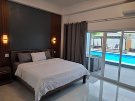 Una habitación de hotel moderna con una cama grande, vista a una piscina y puerta corrediza de vidrio.
