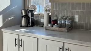 A kitchen with white cabinets, a coffee maker, water bottles, and decorative mugs on shelves. - Your Toledo Bend Lakefront Home – Neighborhood Boat Launch Just Next Door (Many)