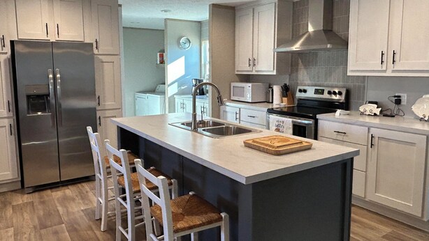 A modern kitchen with white cabinets, stainless steel appliances, a central island with bar stools, and a large window. - Your Toledo Bend Lakefront Home – Neighborhood Boat Launch Just Next Door (Many)