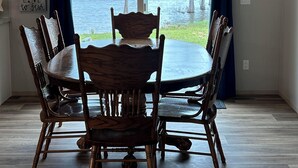 A dining area with a round table and six wooden chairs, large windows with curtains, and two wall signs. - Your Toledo Bend Lakefront Home – Neighborhood Boat Launch Just Next Door (Many)