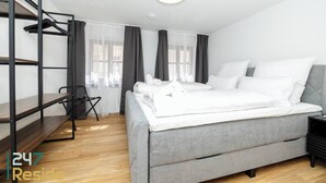 A modern hotel room with a bunk bed, a grey sofa bed, a small desk, and a chair. - 247 Reside: Apartment SZ2 | Downtown | Netflix (Straubing)