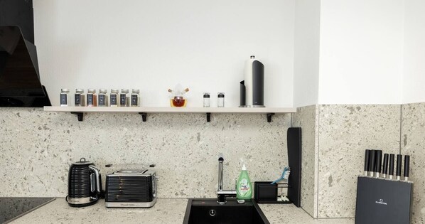 A kitchen with a granite countertop, a coffee maker, a toaster, a sink, and a knife block. - 247 Reside: Apartment SZ2 | Downtown | Netflix (Straubing)