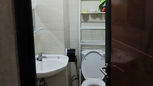 A compact bathroom with a white sink, toilet, and a small shelf with toiletries. - Gateway Pastuer Apartement by Clover  (Cimahi)