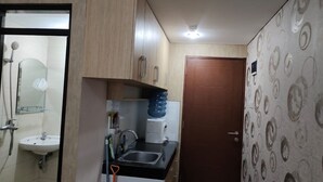 A compact kitchen with a sink, countertop, and a door with a circular pattern. - Gateway Pastuer Apartement by Clover  (Cimahi)