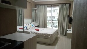 A hotel room with a bed, a desk, and a window with curtains. - Gateway Pastuer Apartement by Clover  (Cimahi)