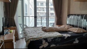 A bedroom with a bed, a desk, and a window with curtains. - Gateway Pastuer Apartement by Clover  (Cimahi)