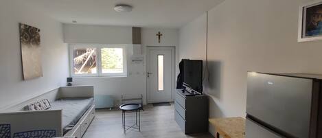 A compact living space with a bed, a small table, a TV, and a refrigerator.