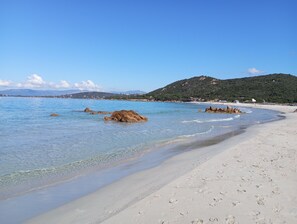 Ein Strand mit klarem, blauem Wasser, sandigem Ufer und Felsformationen.