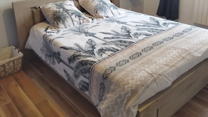 Ein Bett mit gemustertem Überwurf, einem Holzkopfteil und einem an der Wand befestigten Kunstwerk.