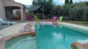 Ein Schwimmbecken mit Steinsims, umgeben von einer Terrassenfläche mit Stühlen und einem Tisch.