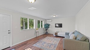 Ein geräumiges Wohnzimmer mit Holzböden, einem großen Teppich, einer Couch und einem an der Wand befestigten Fernseher.