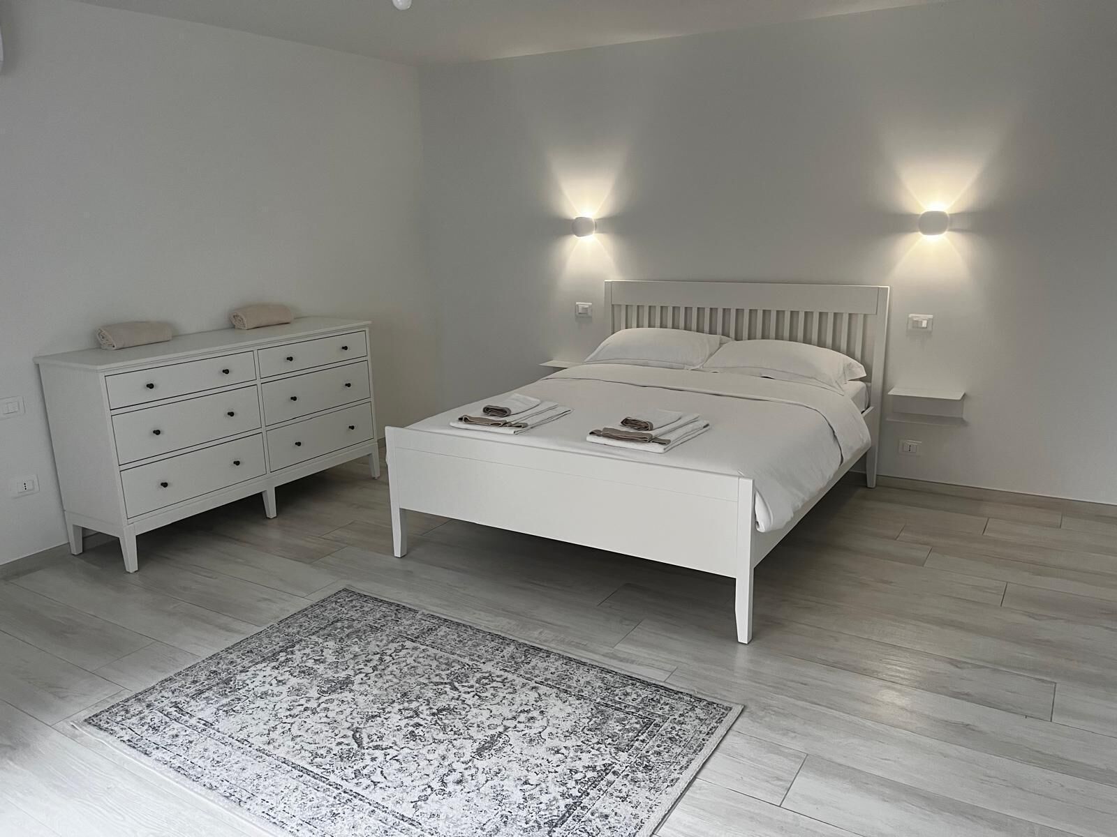 A bedroom with a white bed, a dresser, and a rug.