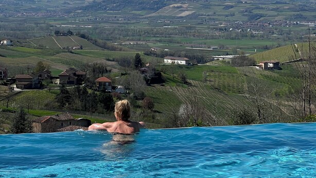 A person in a swimming pool with a view of a mountainous landscape in the background. - Spectacular views of UNESCO Castles, Langhe valley, French, Italian & Swiss alps (Costigliole di Asti)