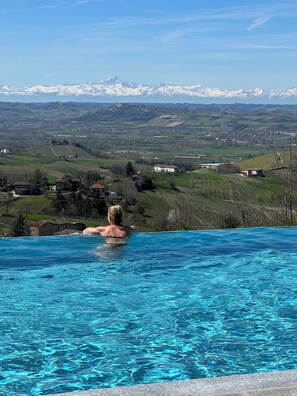 A person in a swimming pool with a view of a mountainous landscape in the background. - Spectacular views of UNESCO Castles, Langhe valley, French, Italian & Swiss alps (Costigliole di Asti)