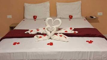 Une chambre d’hôtel avec un lit, du linge de lit blanc, un plaid rouge et une serviette pliée en forme de cœur.