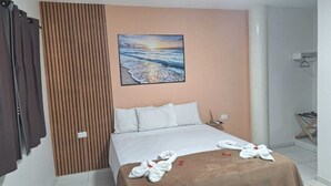 A hotel room with a bed, a painting of a sunset over the ocean, a wooden panel wall, and a towel on the bed. - Pousada Caminho do Paraíso (Ipojuca)