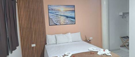 A hotel room with a bed, a painting of a sunset over the ocean, a wooden panel wall, and a towel on the bed.