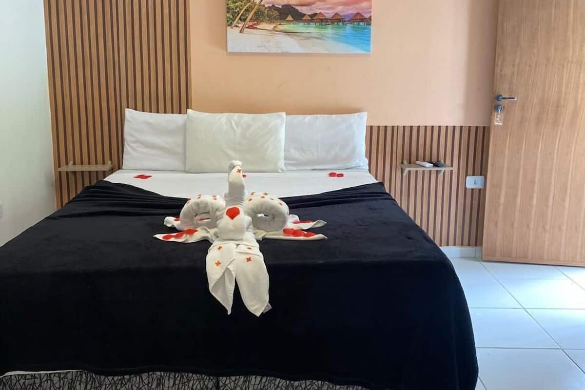 A hotel room with a bed, a painting of a beach scene, and a decorative pillow arrangement.