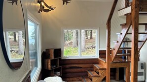 A cozy living room with a wooden staircase, a large mirror, and a view of the outdoors. - Cozy home with a view, newly remodeled. (Homer)