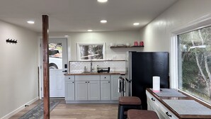 A modern kitchen with white cabinets, a black refrigerator, and a window with a view of trees. - Cozy home with a view, newly remodeled. (Homer)
