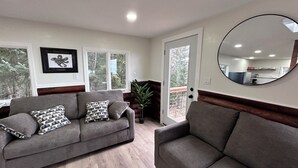A living room with a grey sofa, a round mirror, and a view of the kitchen through a glass door. - Cozy home with a view, newly remodeled. (Homer)