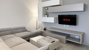 A modern living room with a grey sofa, a coffee table, and a TV mounted on the wall displaying 'NETFLIX'. - Suite Patrizia - Appartamento nel Cuore di Modena (Modena)